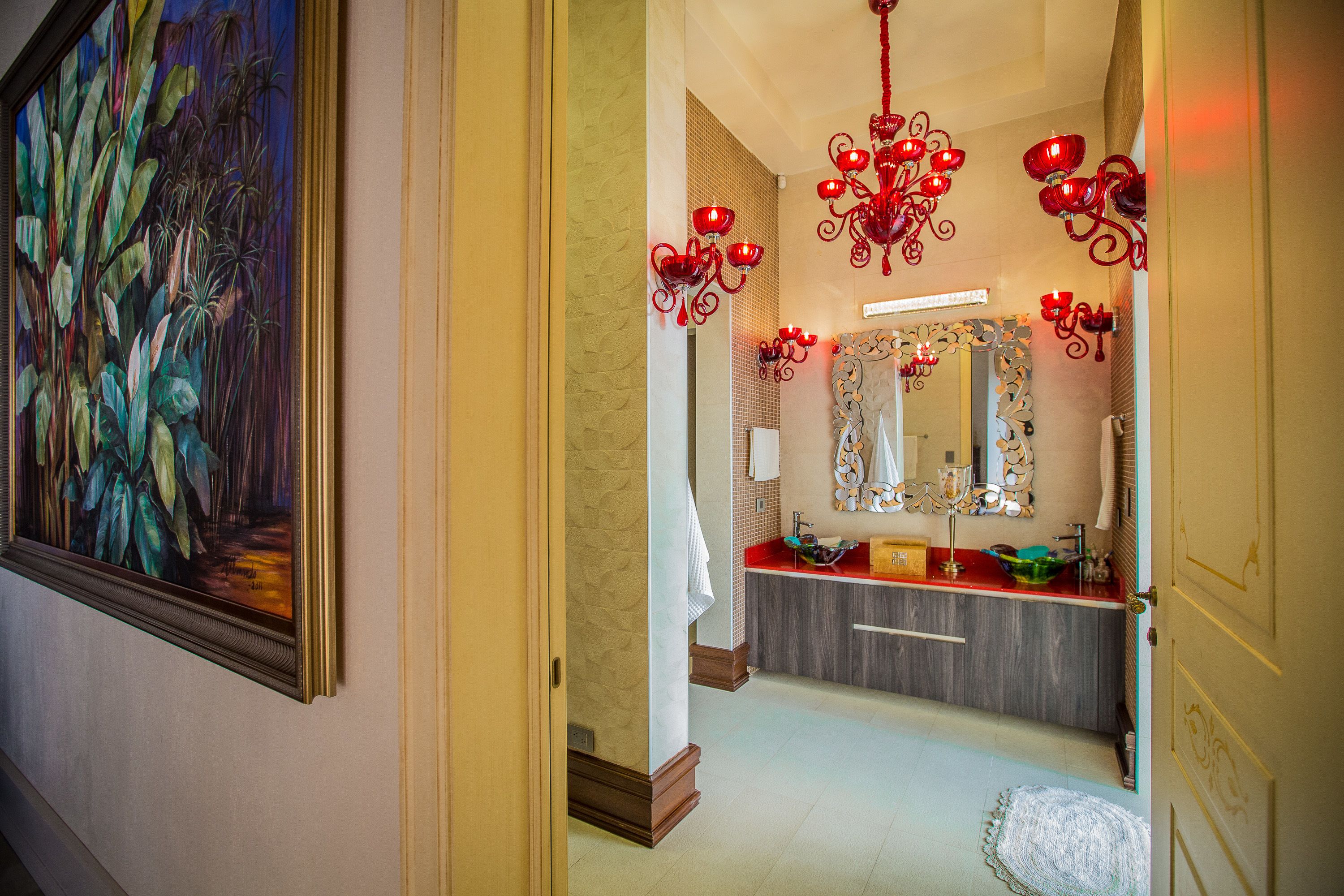 Une salle de bain avec un lustre rouge, un grand miroir et un tableau accroché au mur.
