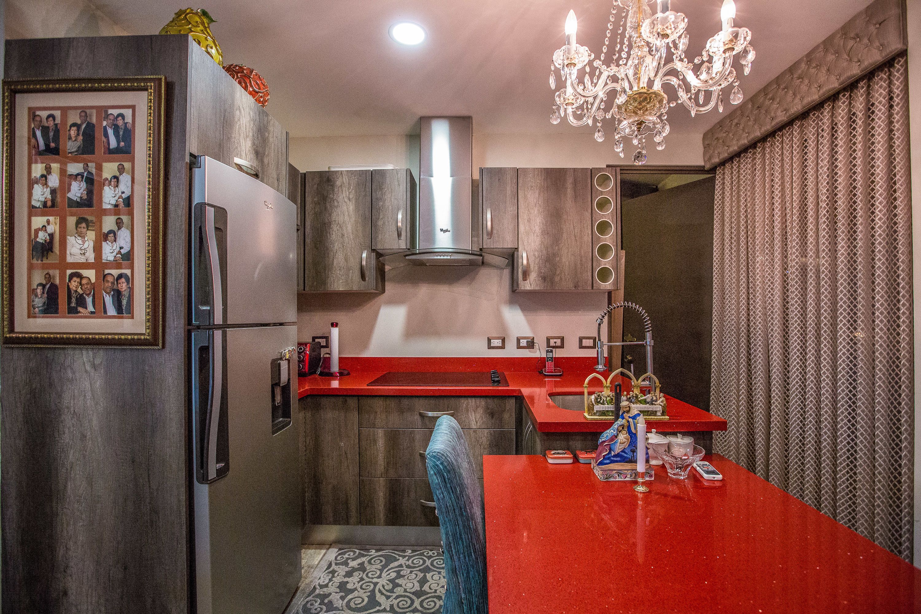 A modern kitchen with a stainless steel refrigerator, a red countertop, and a chandelier.
