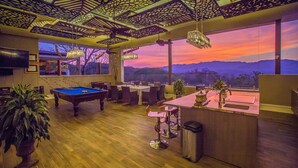 A pool table, bar area, and large windows with a view of mountains at sunset. - La Toscana Hills (Atenas)