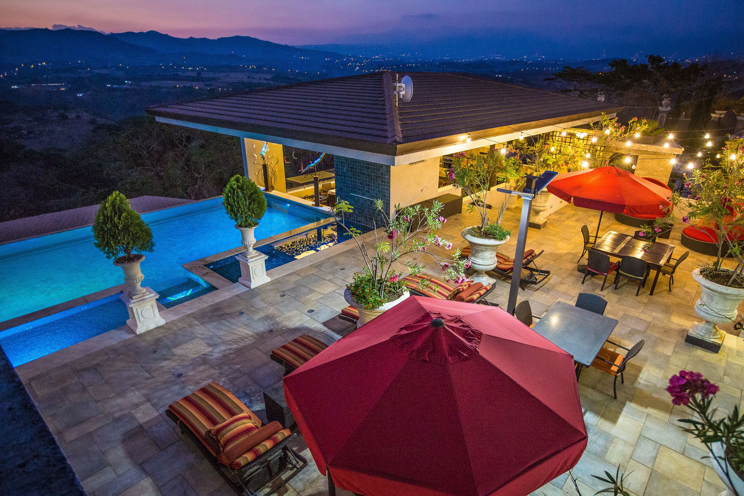 A rooftop pool area with a dining setup and a view of the landscape.