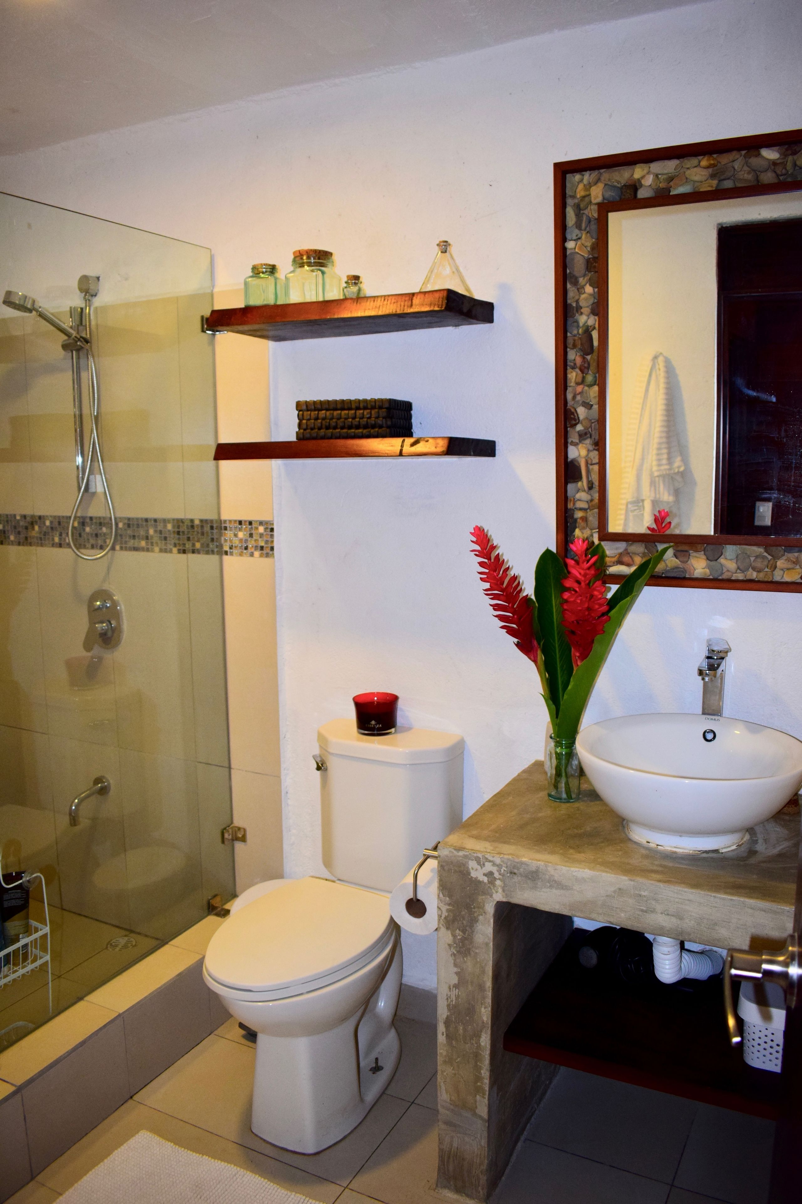 A bathroom with a glass-enclosed shower, a toilet, a sink, and shelves above the toilet.