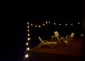 En udendørs terrasse med lyskæder, hvide loungesenge og et lille bord.