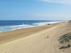 A wide sandy beach with gentle waves, a clear sky, and a few people in the distance.