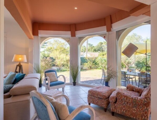 A sunlit room with a sofa, armchairs, and a dining area with a table and chairs.