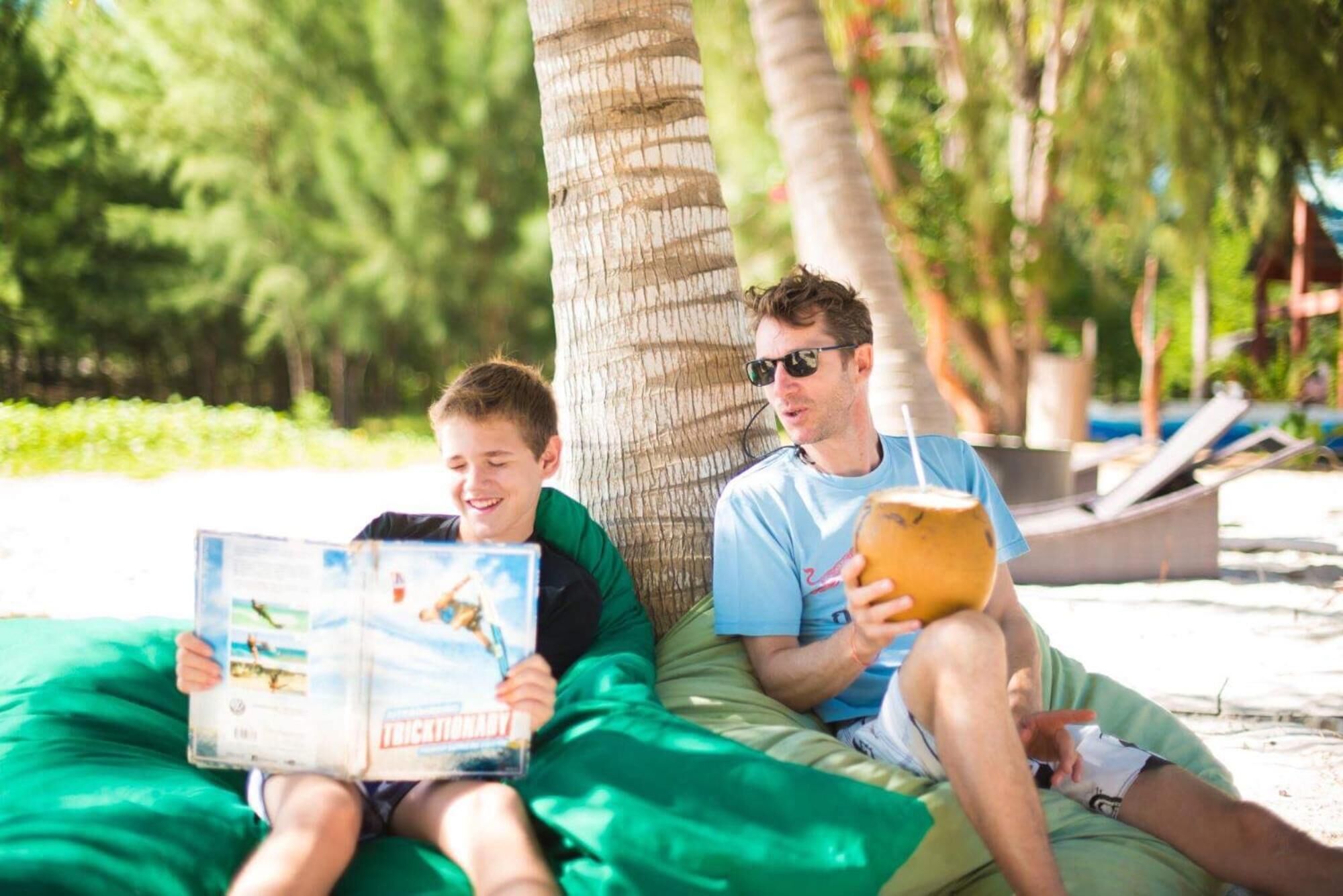 Two people sitting on a green couch outdoors, reading a book and holding a drink.