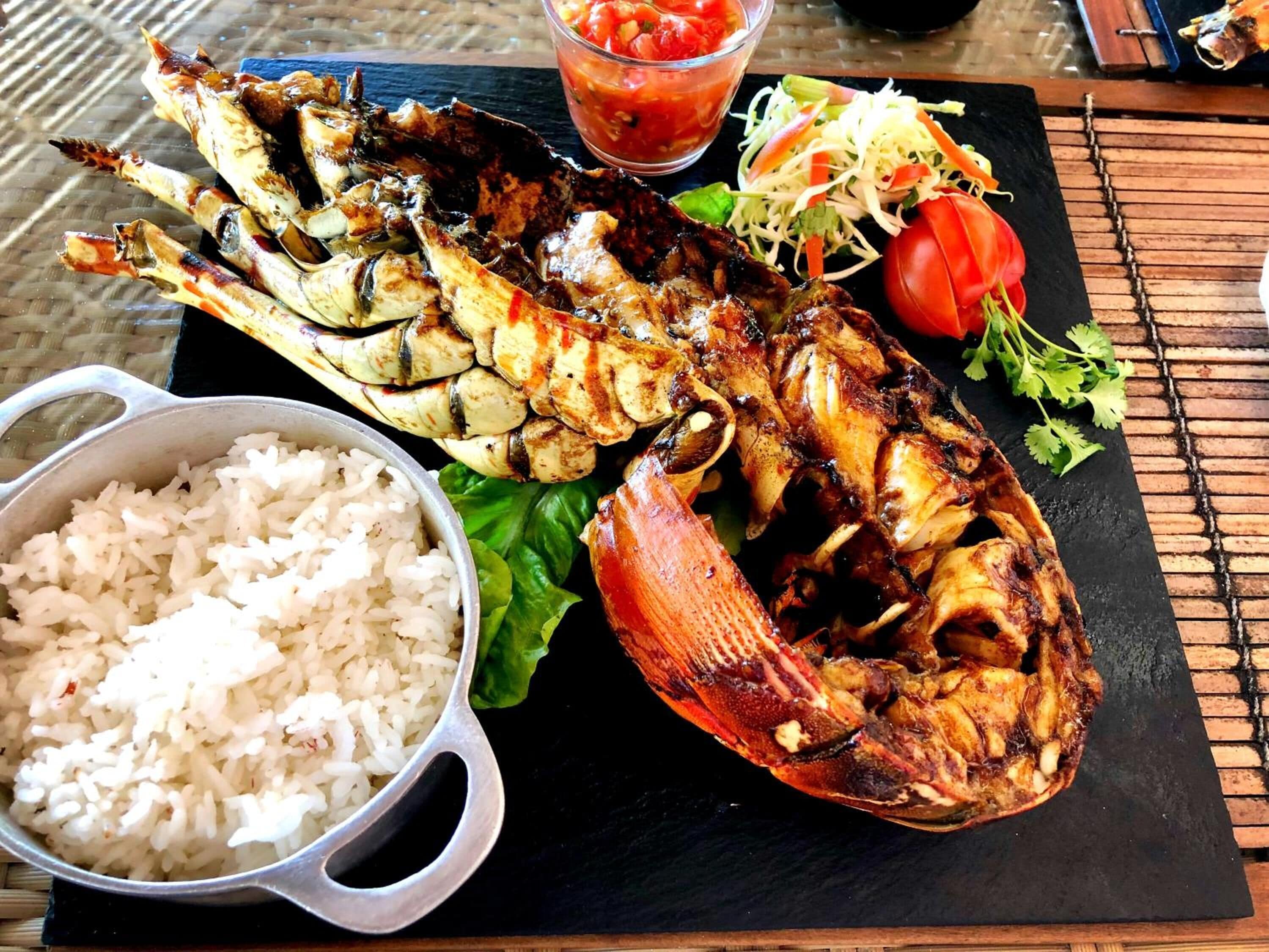 A meal consisting of grilled fish, rice, and a salad with a tomato and cucumber.