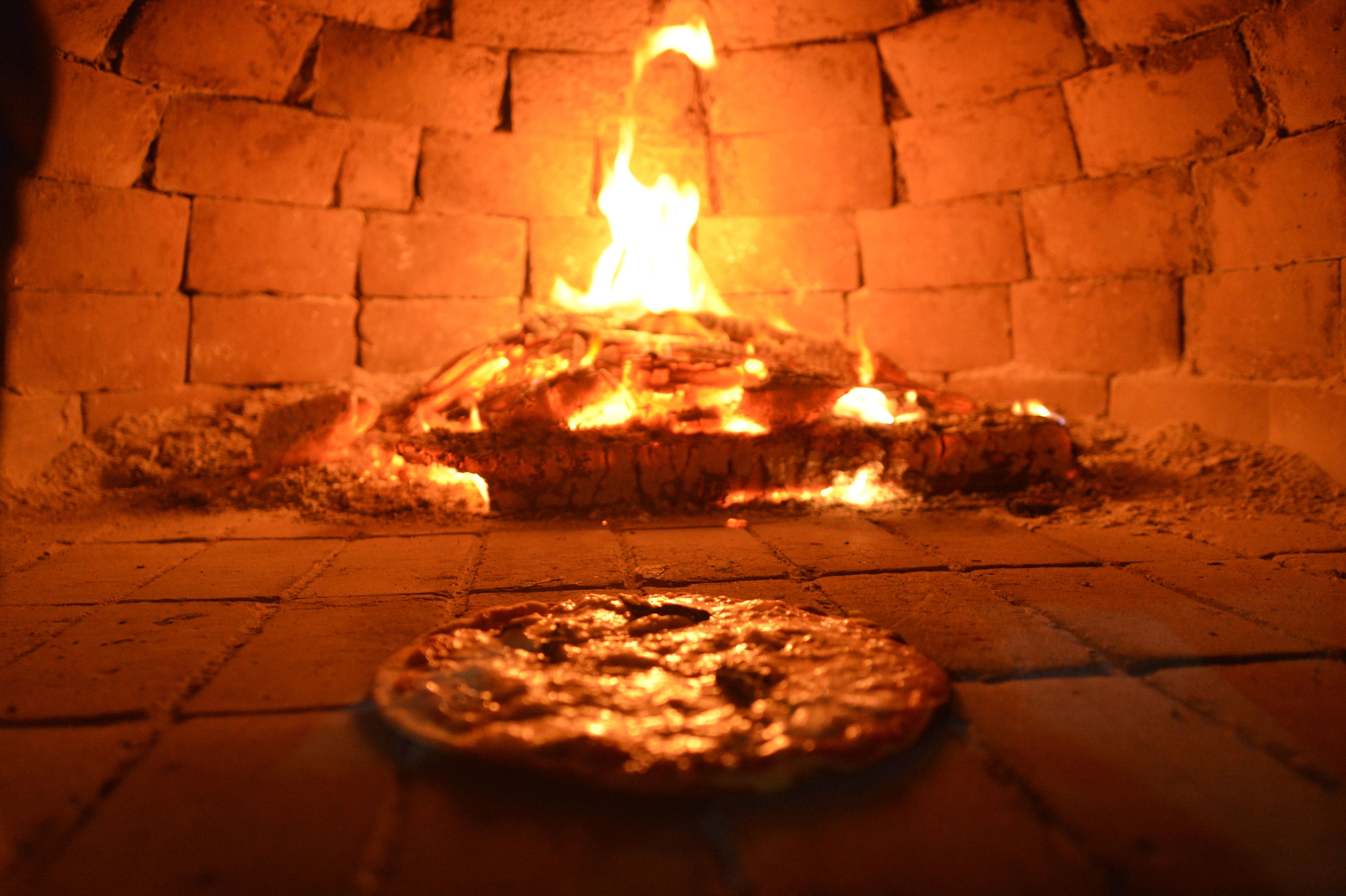 A pizza in a brick oven with flames above it.