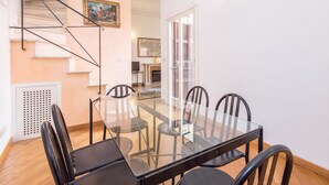 A dining area with a glass table and chairs, a staircase, and a painting on the wall.