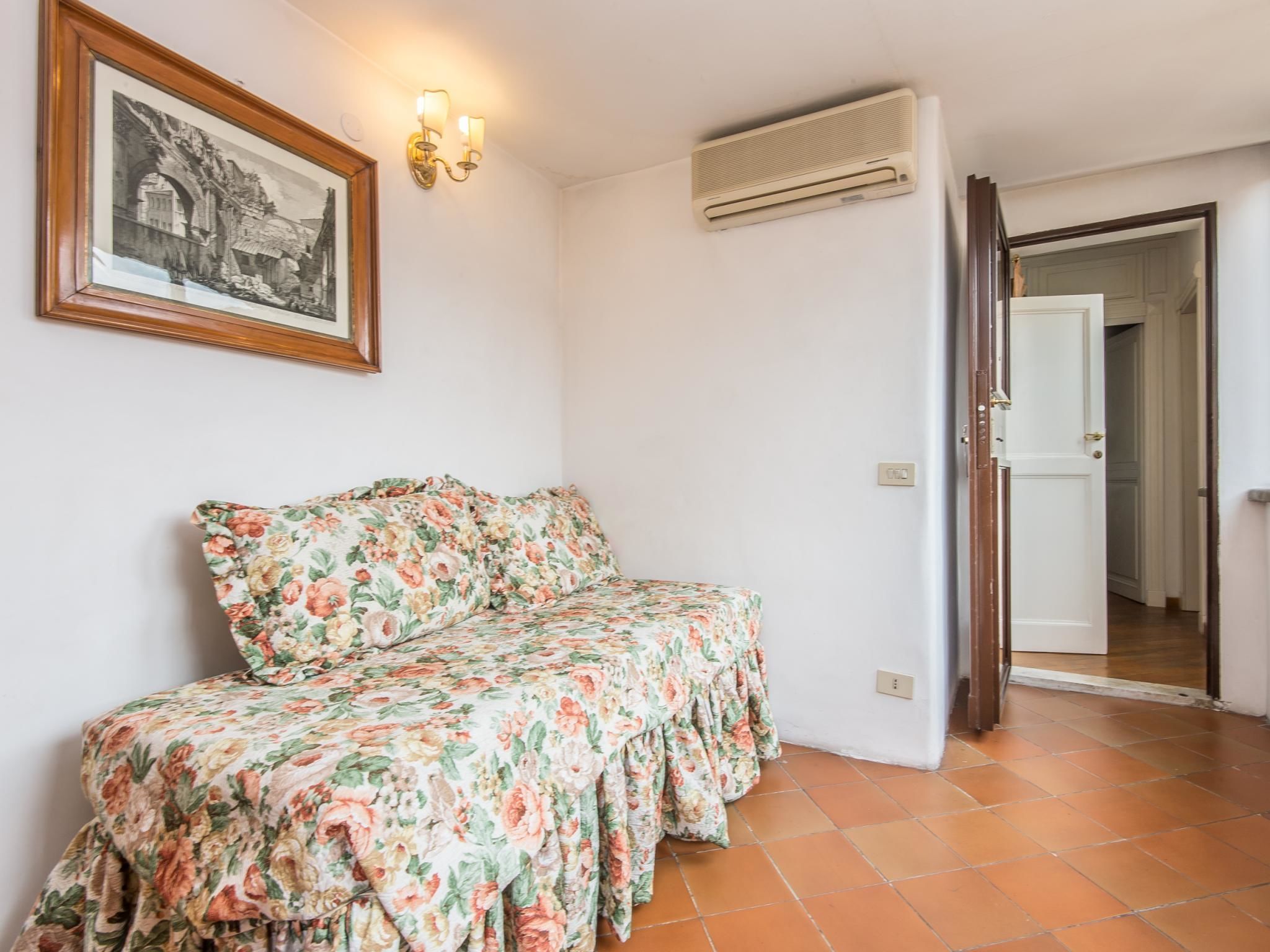 A room with a floral bedspread, a framed picture on the wall, and an air conditioning unit.