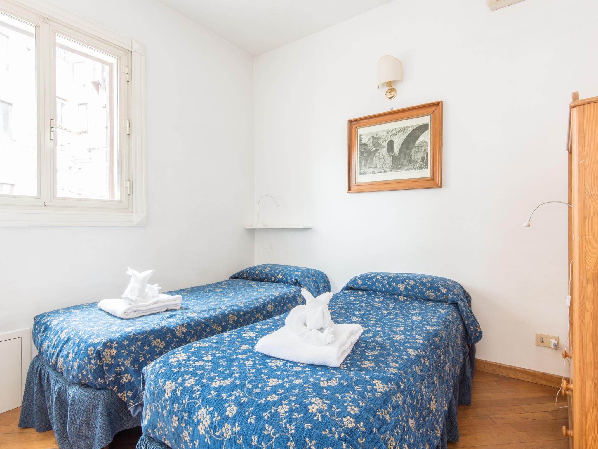 Une chambre avec deux lits simples, un tableau encadré au mur et une fenêtre donnant sur des immeubles.