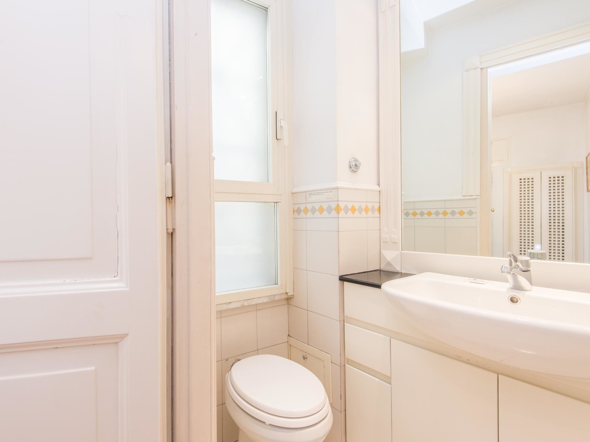 Een badkamer met een wit toilet, een wastafel met een spiegel erboven en een raam met geëtste glas.