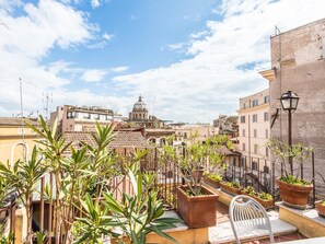 A rooftop terrace with potted plants, a white chair, and a view of a historic building with a dome. - RSH Pallaro Terrace Stunning View (Rome)