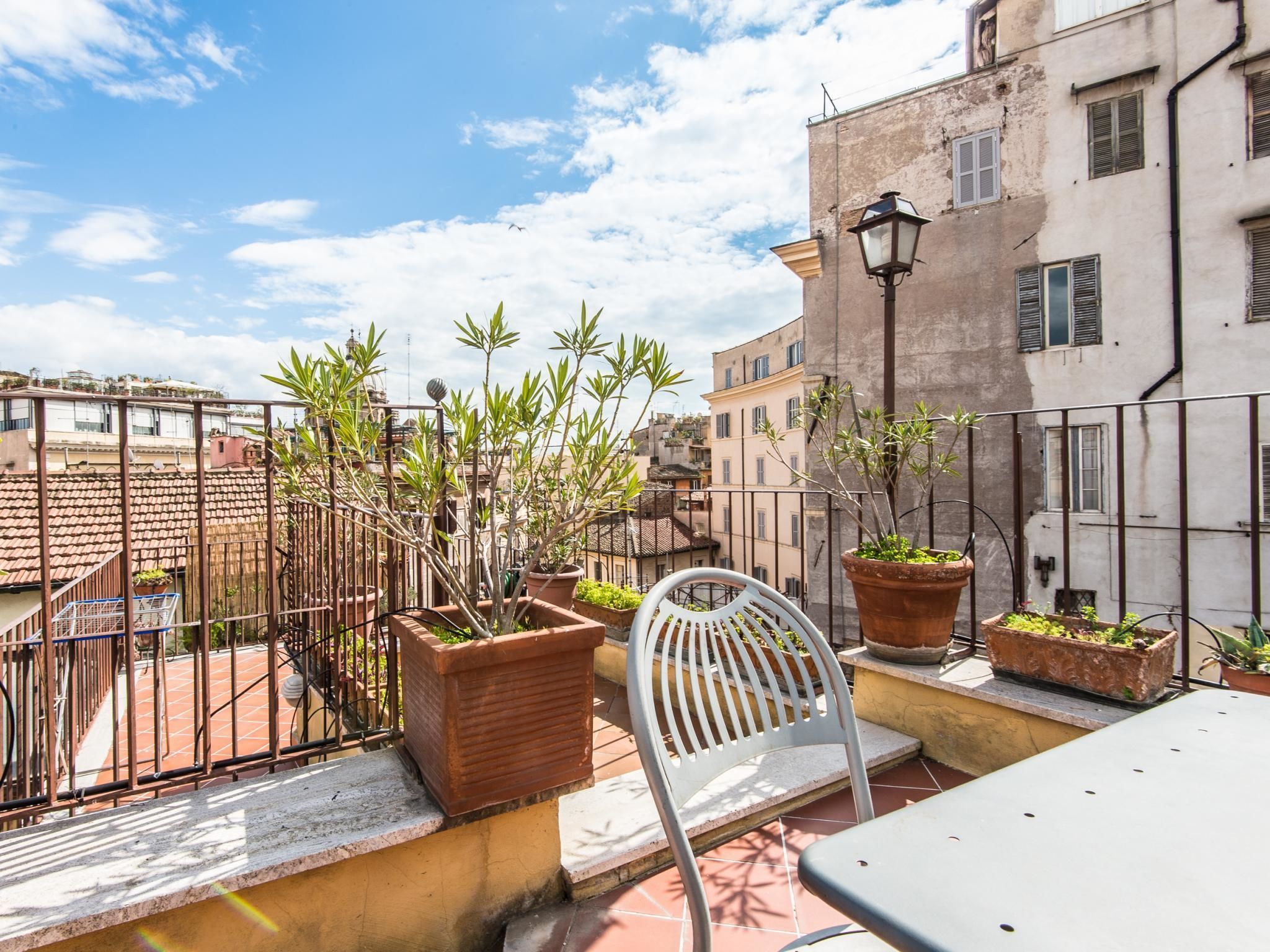 Una terraza en la azotea con plantas en macetas, una silla de metal y una mesa.