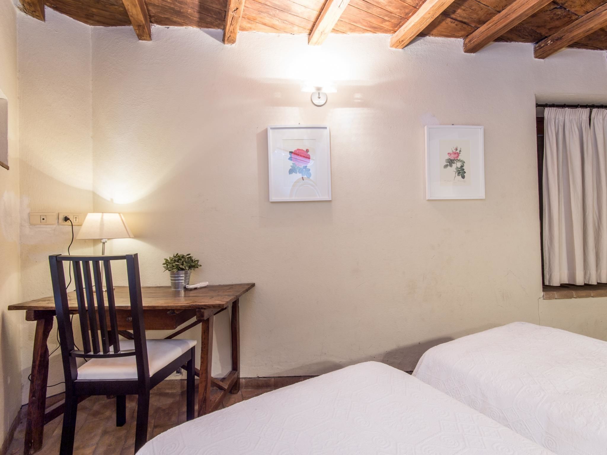 Une chambre avec deux lits, un bureau en bois avec une chaise, une lampe et deux tableaux encadrés au mur.
