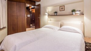 A bedroom with a wooden ceiling, a bed with white bedding, a nightstand, a wall-mounted shelf with a lamp and a plant, and a door leading to another room. - RSH Elegant Apartment Campo dei Fiori (Rome)