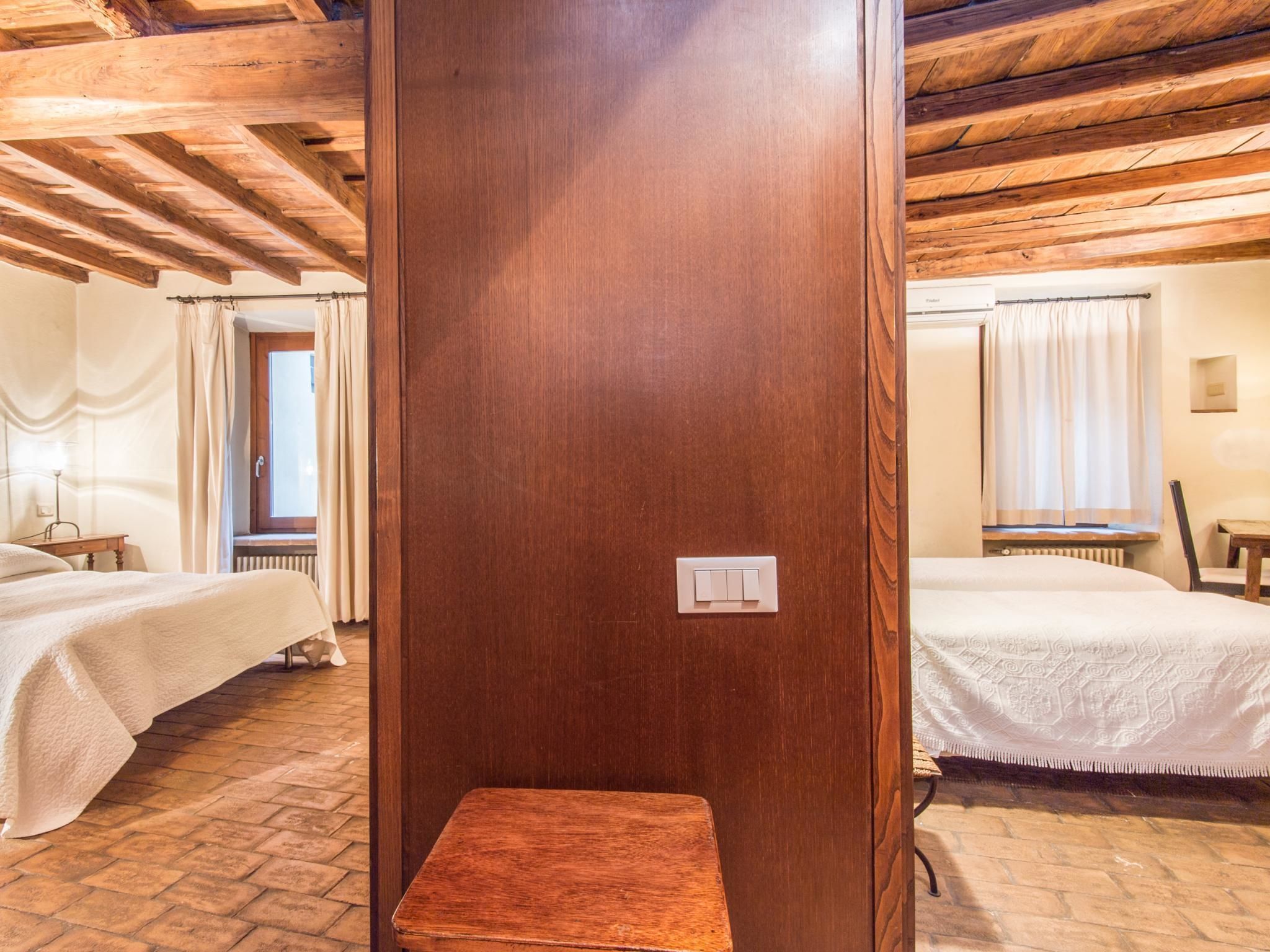 Quarto de hotel com duas camas, um banco de madeira, um radiador e uma janela com cortinas.