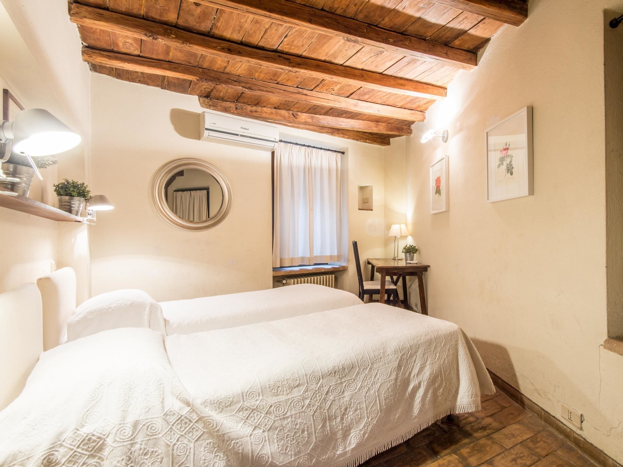 Une pièce chaleureuse avec un plafond en bois, un lit recouvert d’une courtepointe à motifs, une petite table avec une chaise et une fenêtre avec des rideaux.