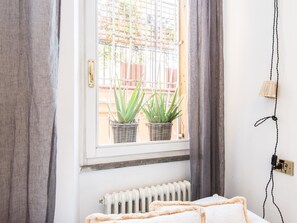 A room with a bed, a radiator, a window with two potted plants, and a curtain. - RSH Luxury Spanish Steps Terrace (Rome)