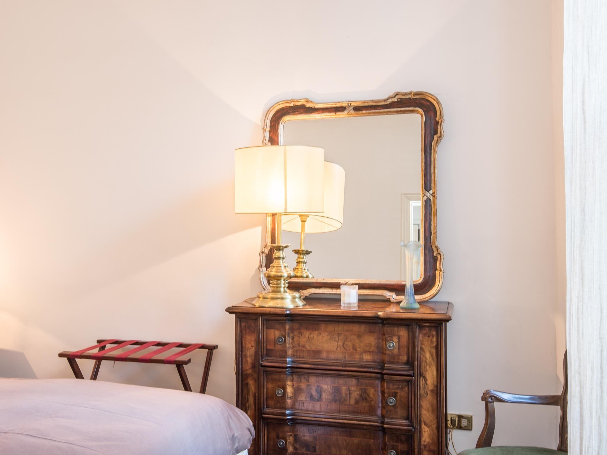 Une chambre d’hôtel avec une commode en bois, un miroir, une lampe, une petite table et une chaise.