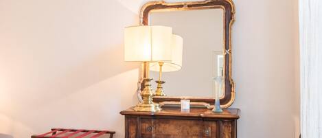 Une chambre d’hôtel avec une commode en bois, un miroir, une lampe, une petite table et une chaise.