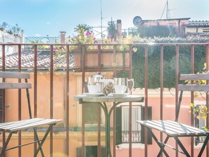 A balcony with a table set for two, a metal fence, and a building with a tiled roof in the background. - RSH Luxury Spanish Steps Terrace (Rome)