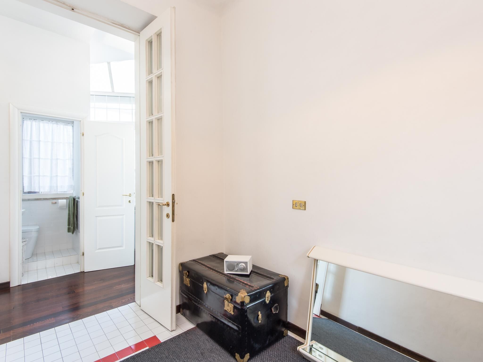 A room with a wooden floor, a white door, a black suitcase, and a small white table.