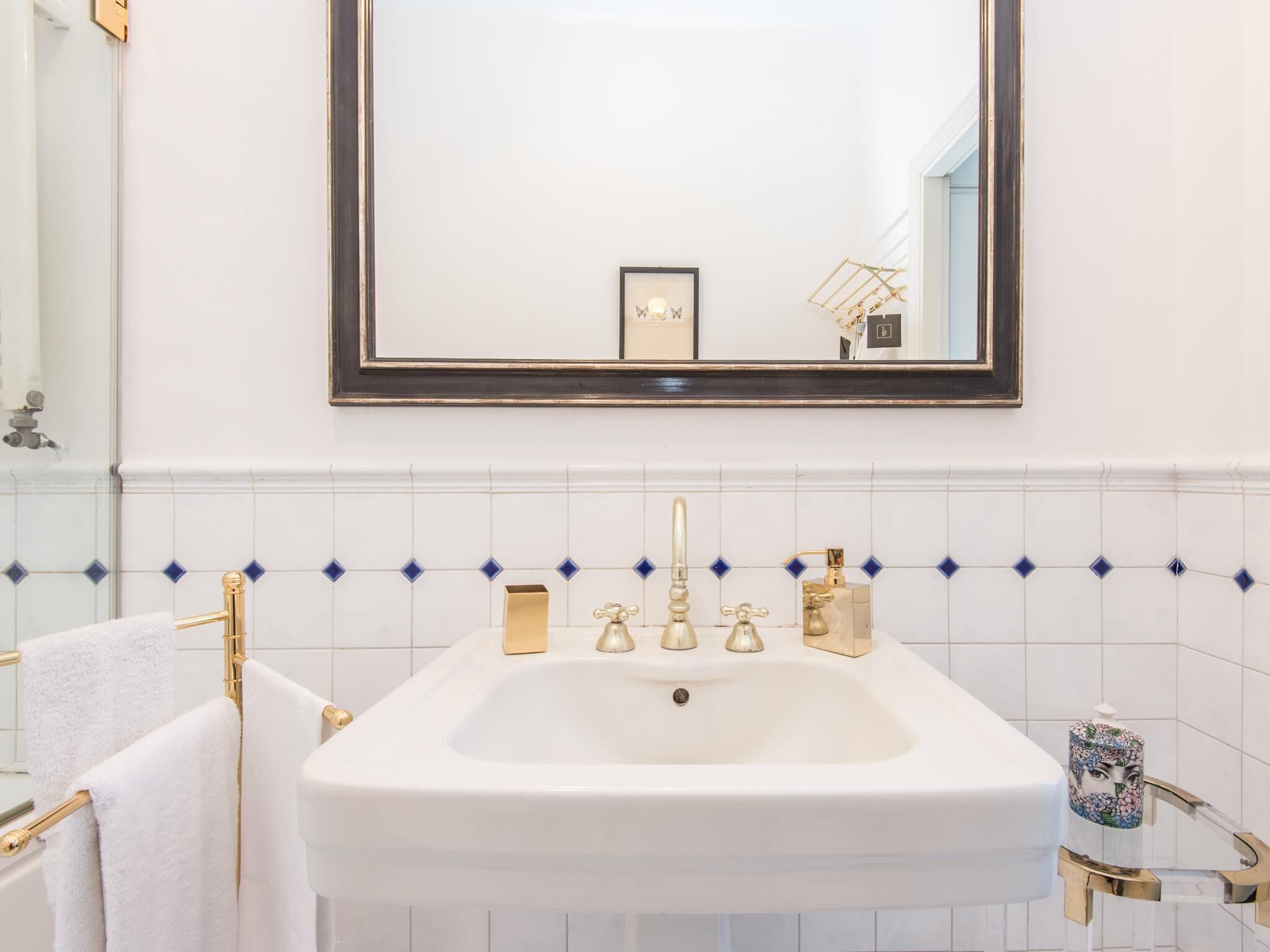 A bathroom with a white sink, gold faucets, and a mirror above it.