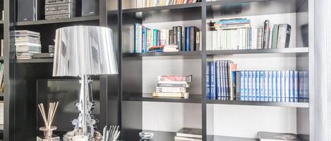 Et moderne bibliotek med sorte reoler fyldt med bøger, et glastæppe med en lampe og en stol.