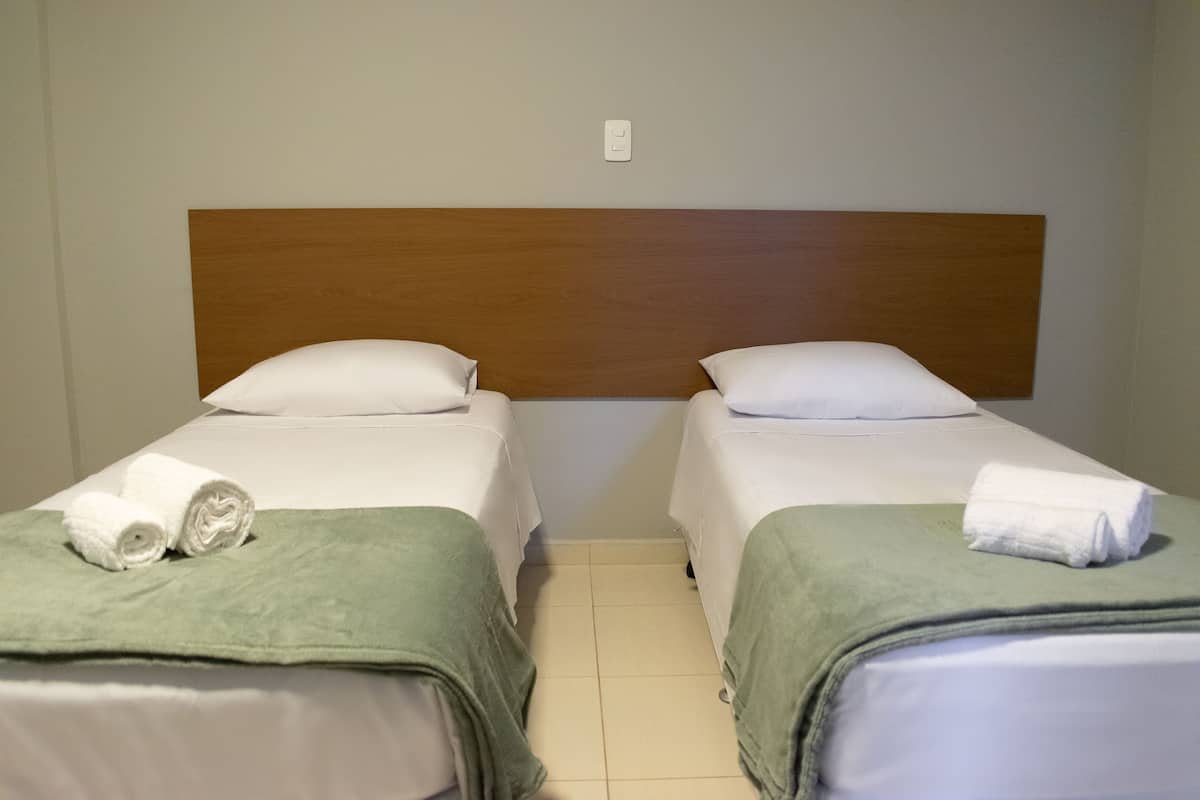 Duas camas de solteiro com cabeceiras de madeira, roupa de cama branca e mantas decorativas verdes.