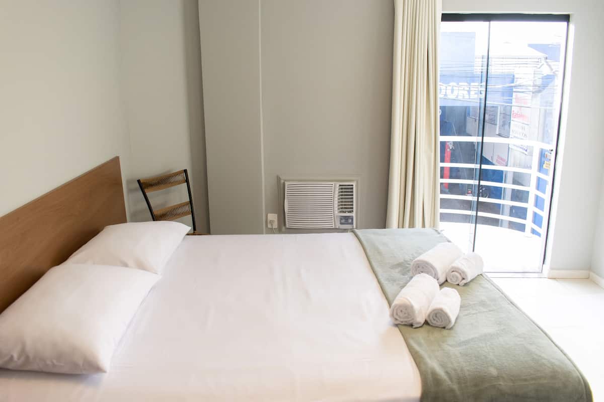 Quarto de hotel com cama, uma cadeira, uma janela e vista para o exterior.