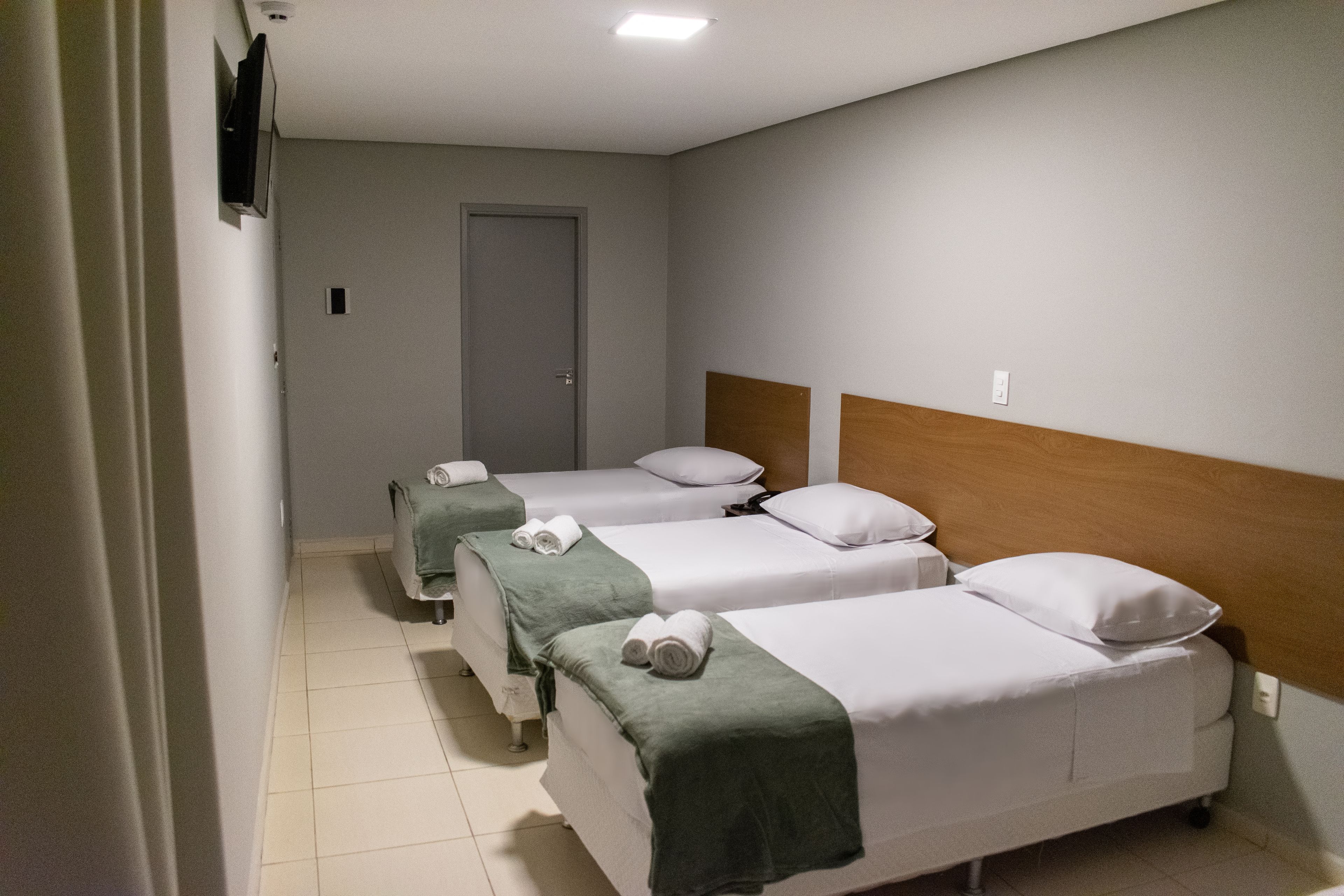 A hotel room with two single beds, a wooden headboard, and a television mounted on the wall.
