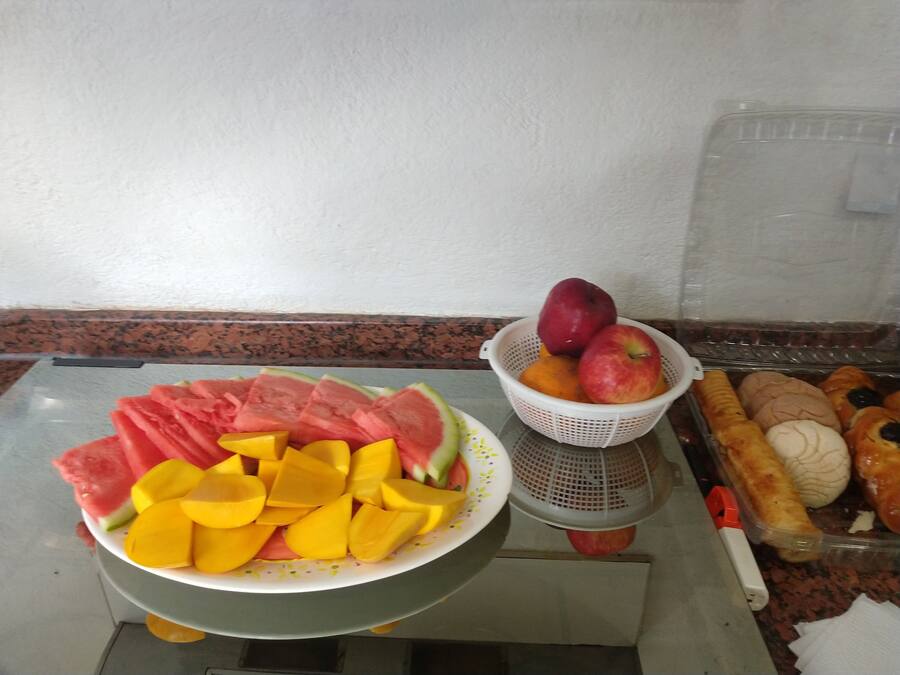 A table with a bowl of sliced fruits and a colander with whole fruits.