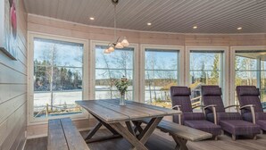 A wooden interior with a large table and chairs, large windows, and a ceiling with wooden beams. - Riemukaari by Interhome (Pertunmaa)