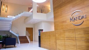 Un hall d’entrée moderne avec un comptoir d’accueil en bois, un escalier et une enseigne sur laquelle on peut lire « MANDAI ».