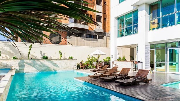 Une piscine avec des chaises longues, un espace patio et un bâtiment doté de grandes fenêtres en arrière-plan.