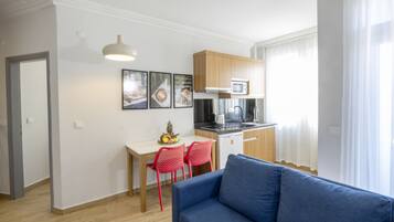 A modern apartment with a kitchenette, a dining area with red chairs, and a blue sofa.