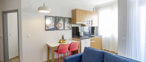 A modern apartment with a kitchenette, a dining area with red chairs, and a blue sofa.