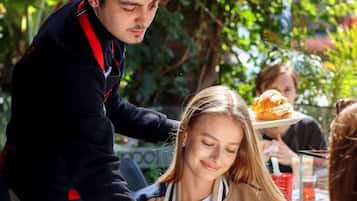 Un groupe de personnes est assis à une table à l’extérieur, devant un menu, avec un chien et un sandwich.
