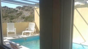 Vista de una piscina con sillas reclinables blancas y un paisaje montañoso al fondo.