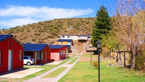 Una hilera de cabañas rojas con un coche estacionado frente a ellas, con un paisaje montañoso de fondo.