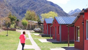 Una hilera de edificios rojos con techos metálicos, un sendero y montañas al fondo.