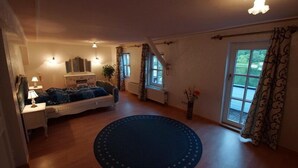 Una camera accogliente con un letto, un tavolino con una lampada, una finestra con tende e una porta che dà su uno spazio all'aperto.
