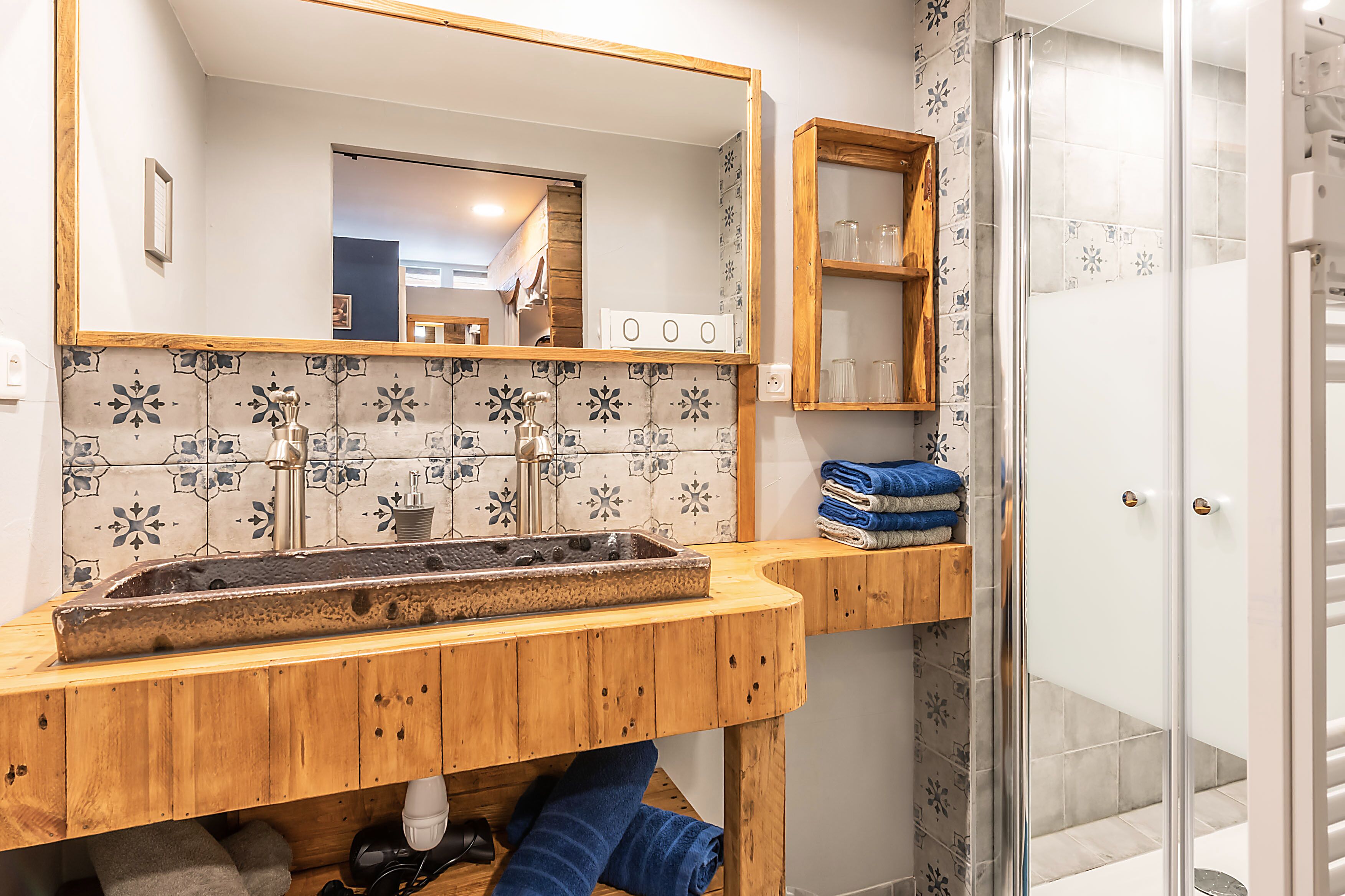 A bathroom with a wooden vanity, a sink with a decorative basin, a mirror, and a shower area.