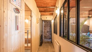 Un pasillo estrecho con paredes de madera y una pared de piedra al final. Hay ventanas a la derecha y una puerta a la izquierda.