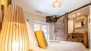 Un dormitorio con cama, cabecera de madera, un ventanal grande, cómoda de madera y espejo.