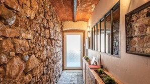 Un pasillo de paredes de piedra con un banco de madera, una puerta que da al exterior y una jardinera en la pared con plantas.