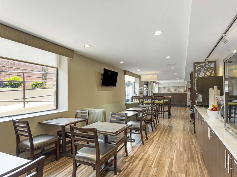 A modern restaurant with wooden tables and chairs, a kitchen area, and a view of the parking lot.