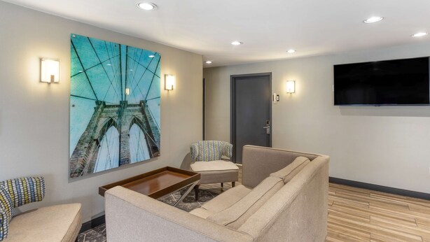 Een moderne hotelkamer met een groot schilderij van een brug, een flatscreen televisie en een zithoek met een bank en twee fauteuils.