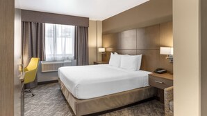 Een hotelkamer met een groot bed, een bureau met stoel, een raam met gordijnen en een wandlamp.