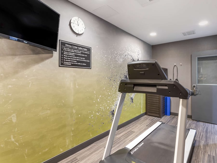 A fitness center with a treadmill, a clock, and a safety rules sign on the wall.